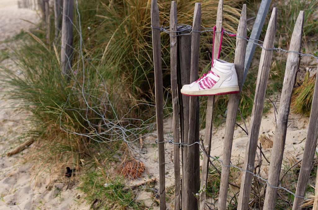 Basket montante suspendue à une clôture de piquet en bois, plantés dans le sable. On devine qu'il s'agit de l'accès à une plage.